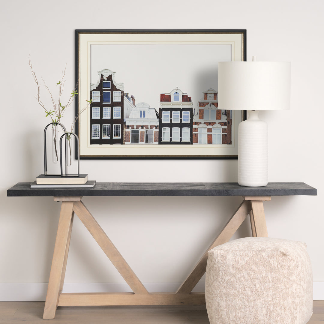 Modern console table with a lamp, vase, and framed artwork in a room.