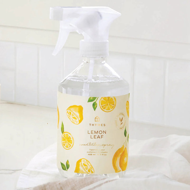 Thymes Clear countertop spray bottle with lemon leaf design on label against a white background