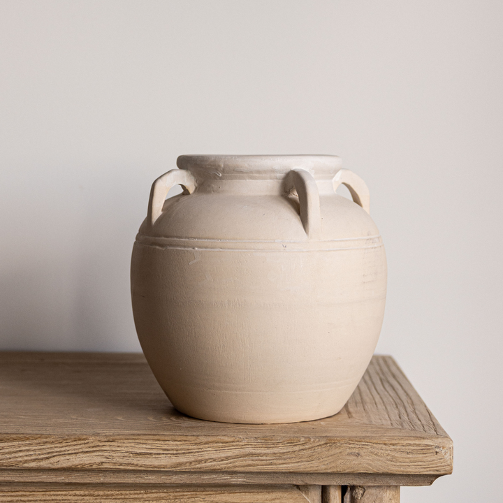 Beige ceramic vase with handles on a wooden surface against a plain background