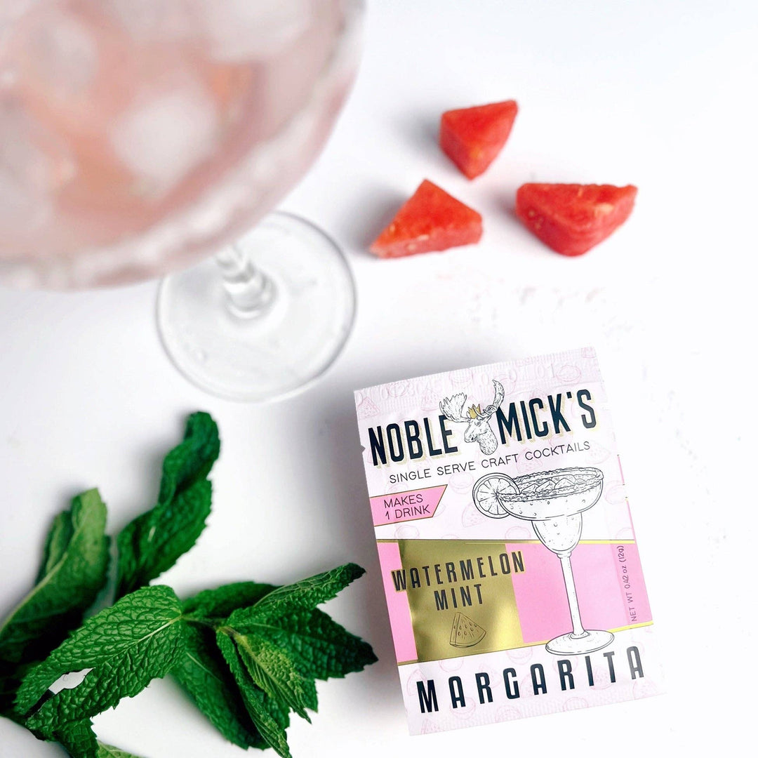 Noble Mick's watermelon mint margarita mix package with a cocktail and ingredients on a white surface