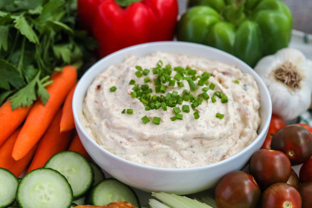 White bowl of garden vegetable dip with green herbs surrounded by vegetables on a white plate