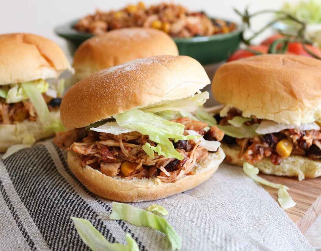 Three pulled pork sandwiches on buns with lettuce and onions, served on a wooden board.