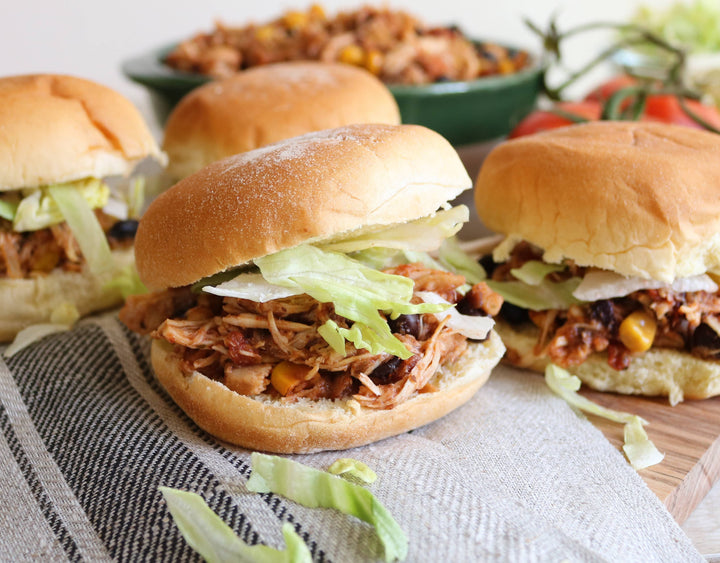 Three pulled pork sandwiches on buns with lettuce and onions, served on a wooden board.