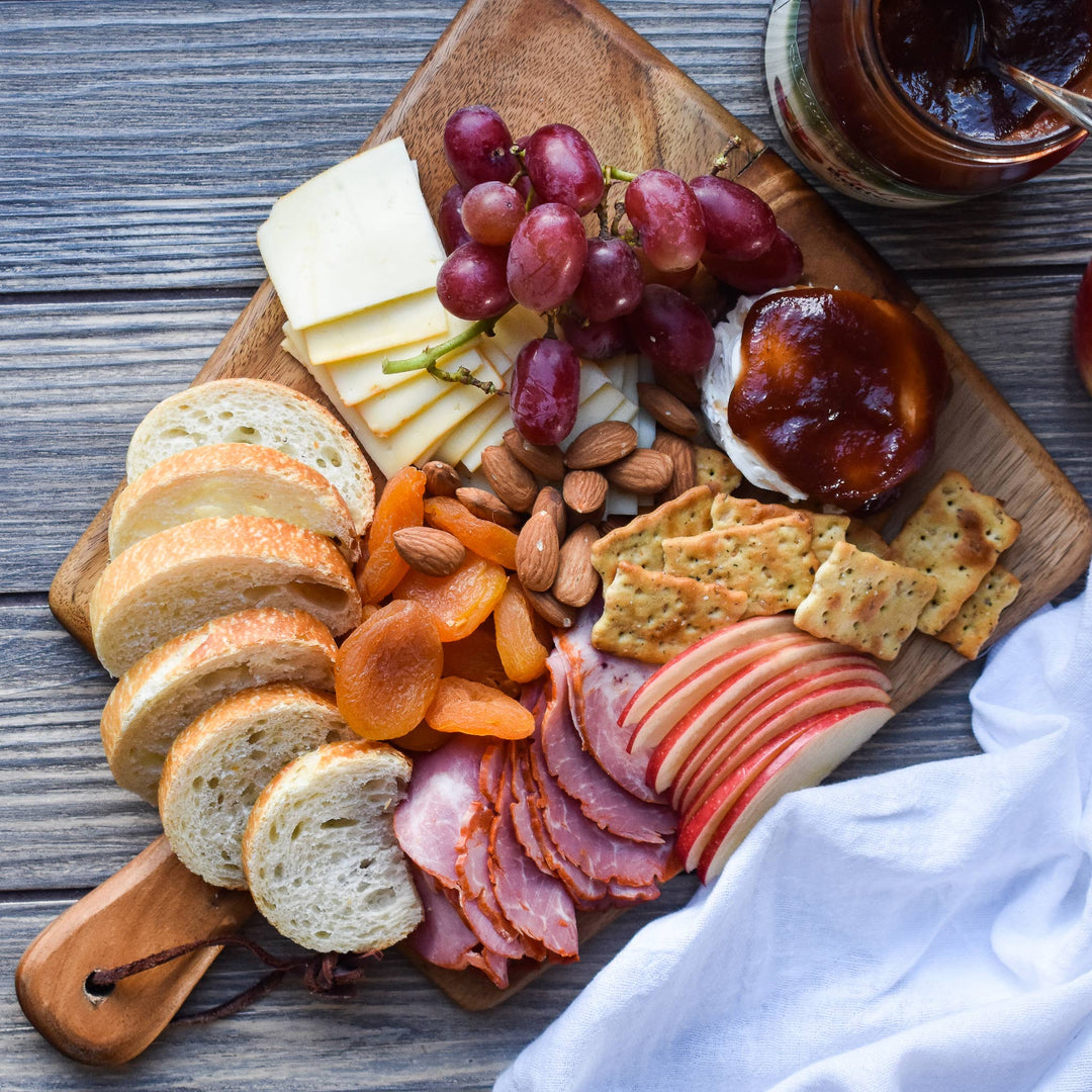 Wooden charcuterie board with bread, cheese, fruits, and meats on a wooden surface.