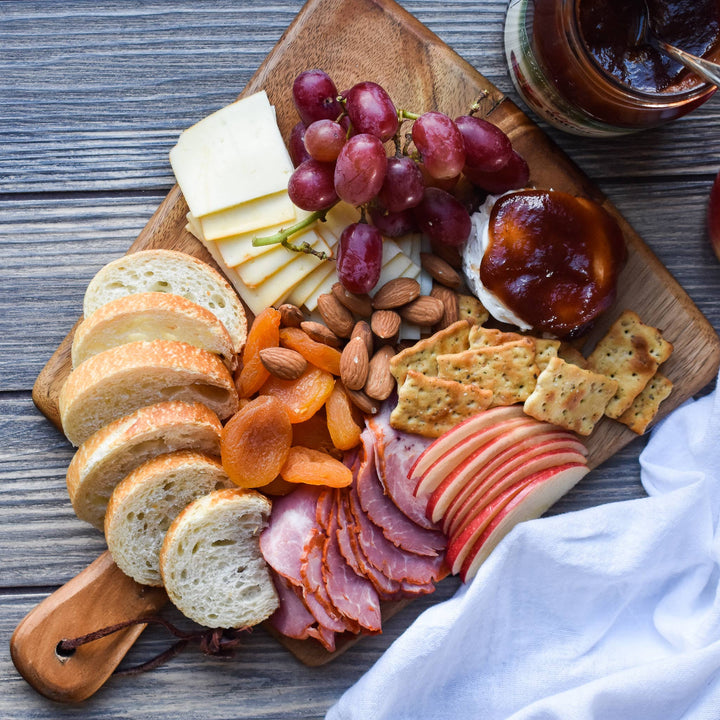 Wooden charcuterie board with bread, cheese, fruits, and meats on a wooden surface.