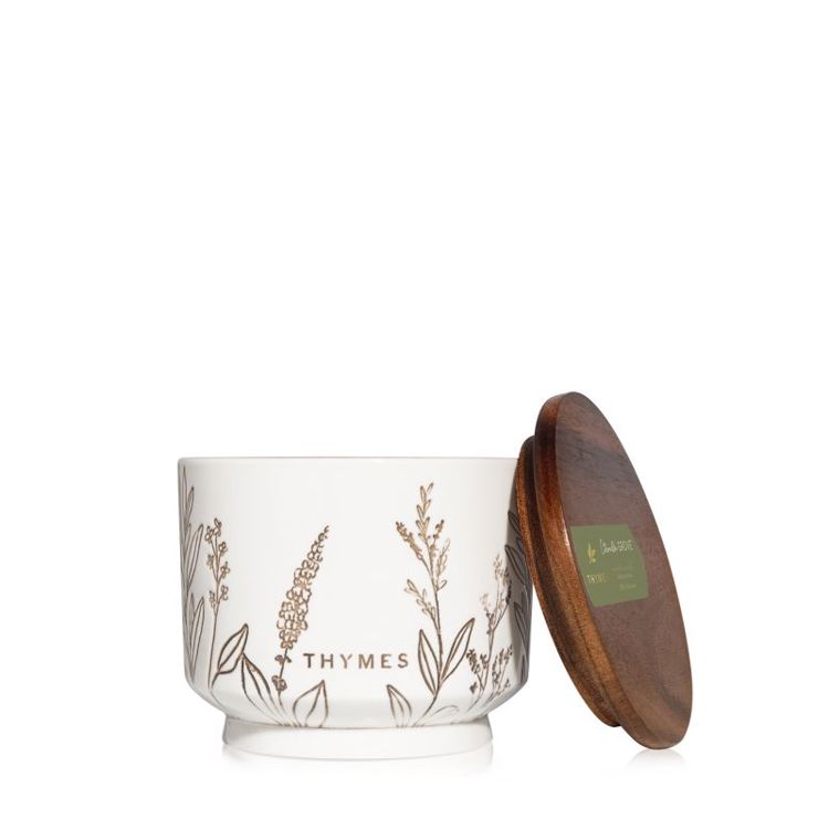 White  citronella candle jar with floral designs and a wooden lid on a white background