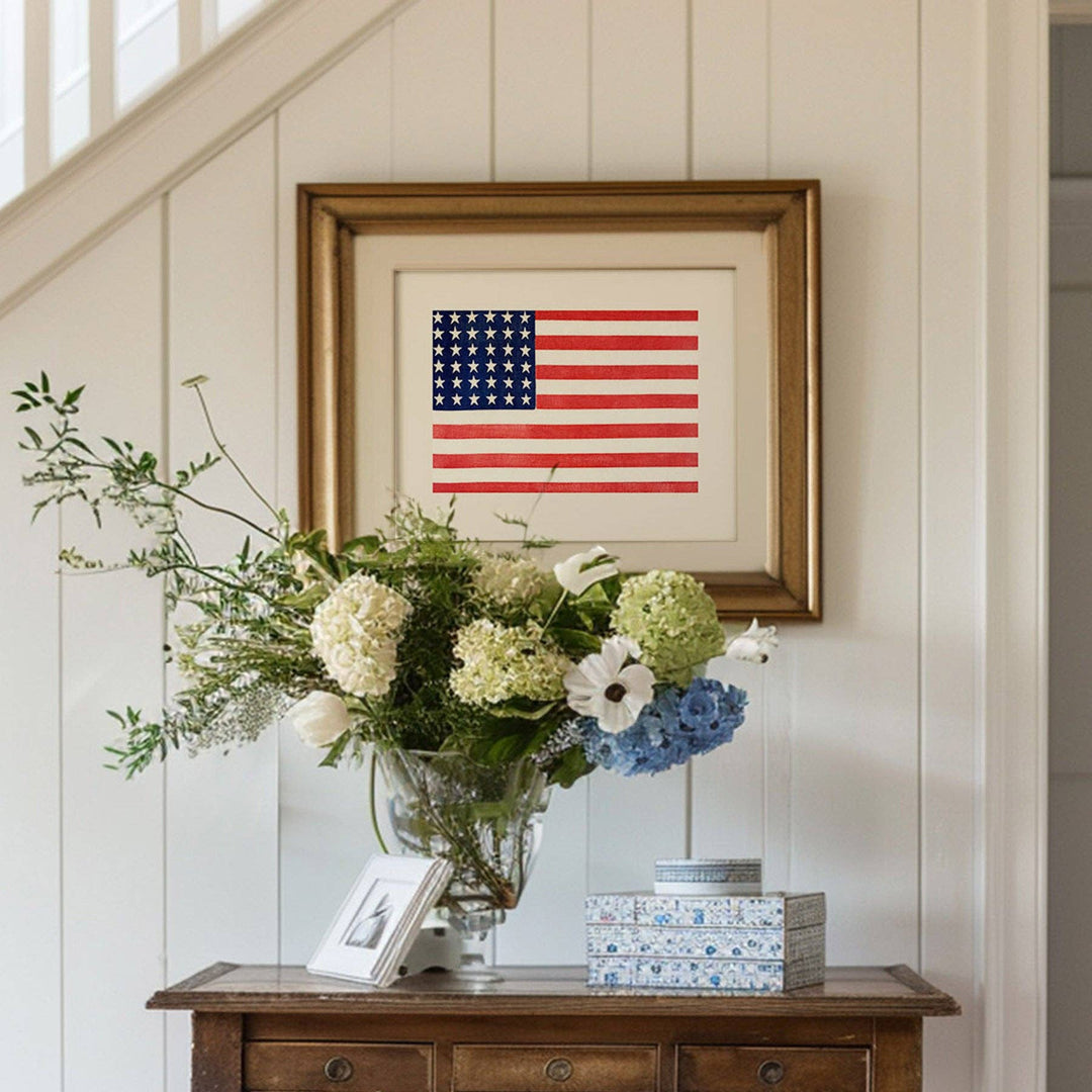 Framed American flag above a wooden console table with flowers and books.