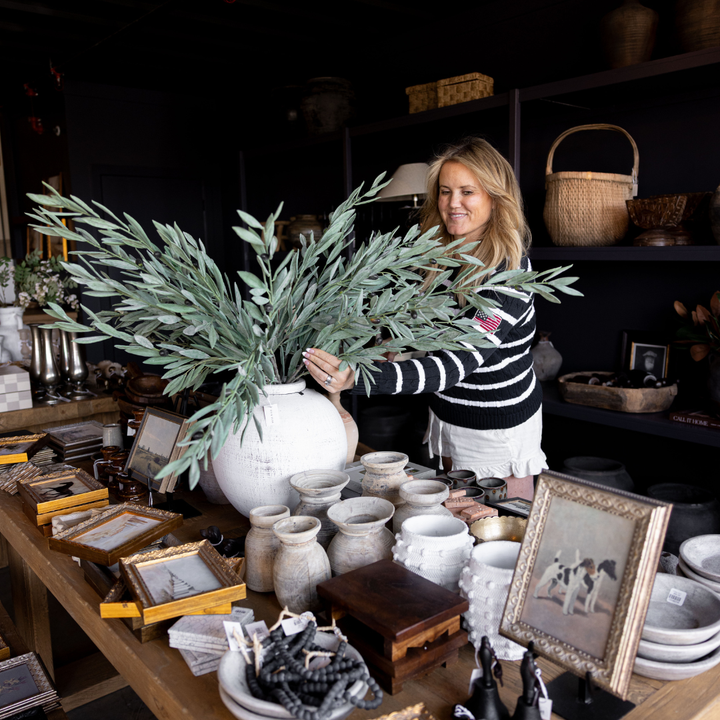 Woman holding a large green plant in a store with various items on display.