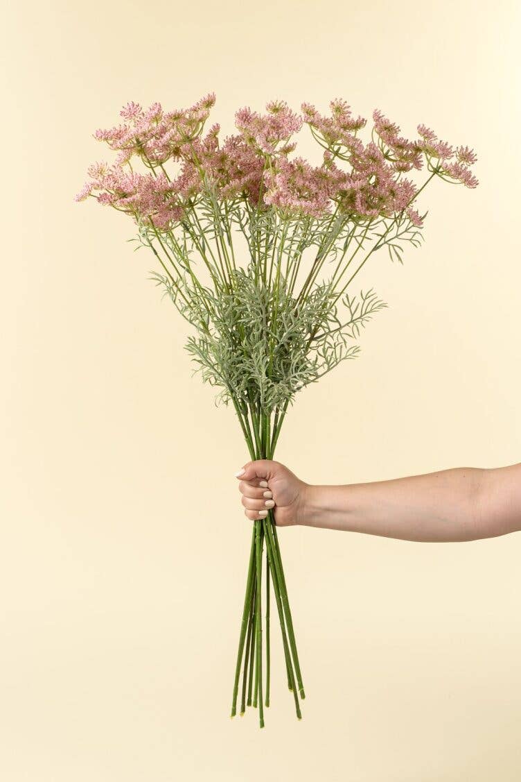 Hand holding a bouquet of pink flowers against a beige background