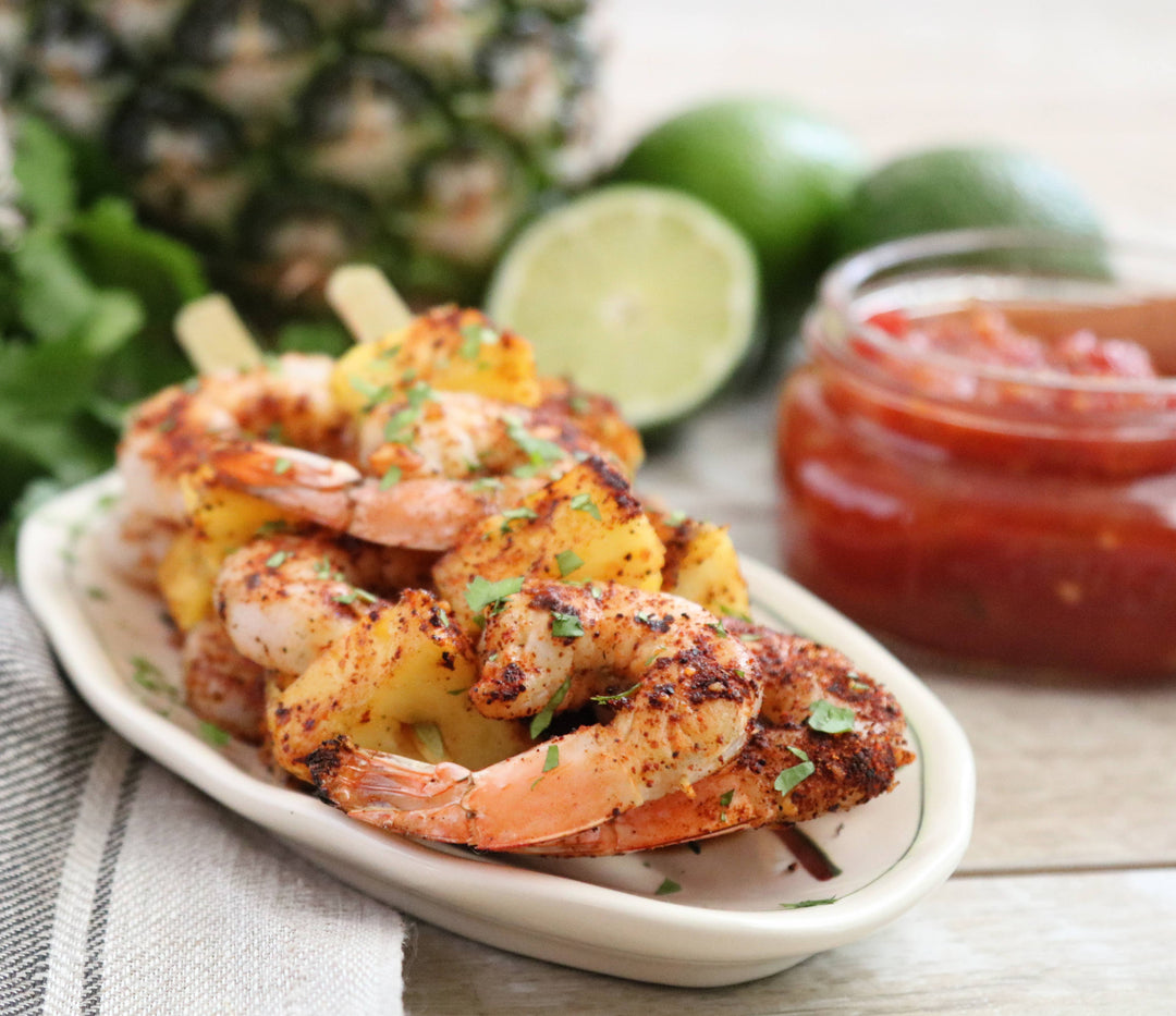 Platter of grilled shrimp skewers with pineapple, lime, and salsa on a wooden surface.