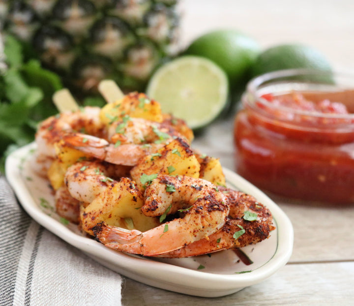 Platter of grilled shrimp skewers with pineapple, lime, and salsa on a wooden surface.