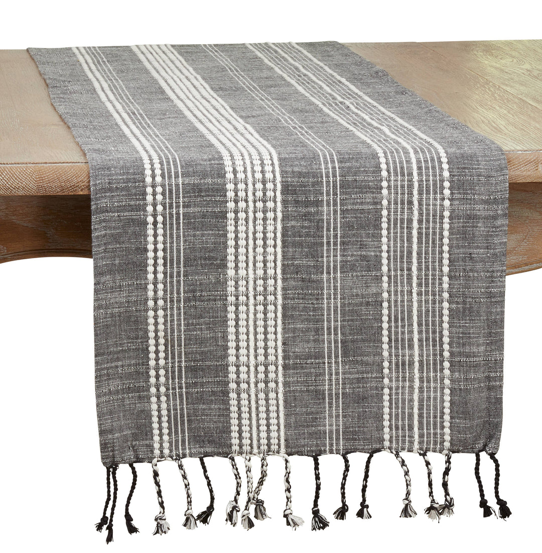 Gray and white striped table runner with tassels on a wooden table.