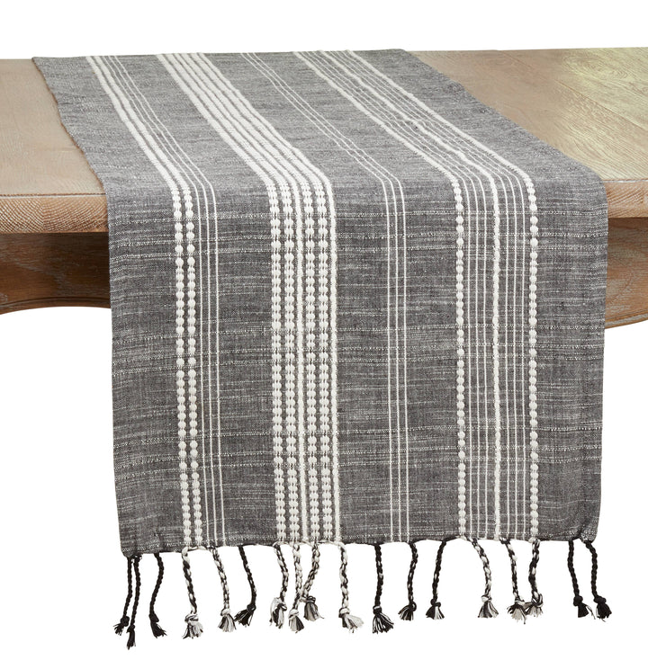 Gray and white striped table runner with tassels on a wooden table.