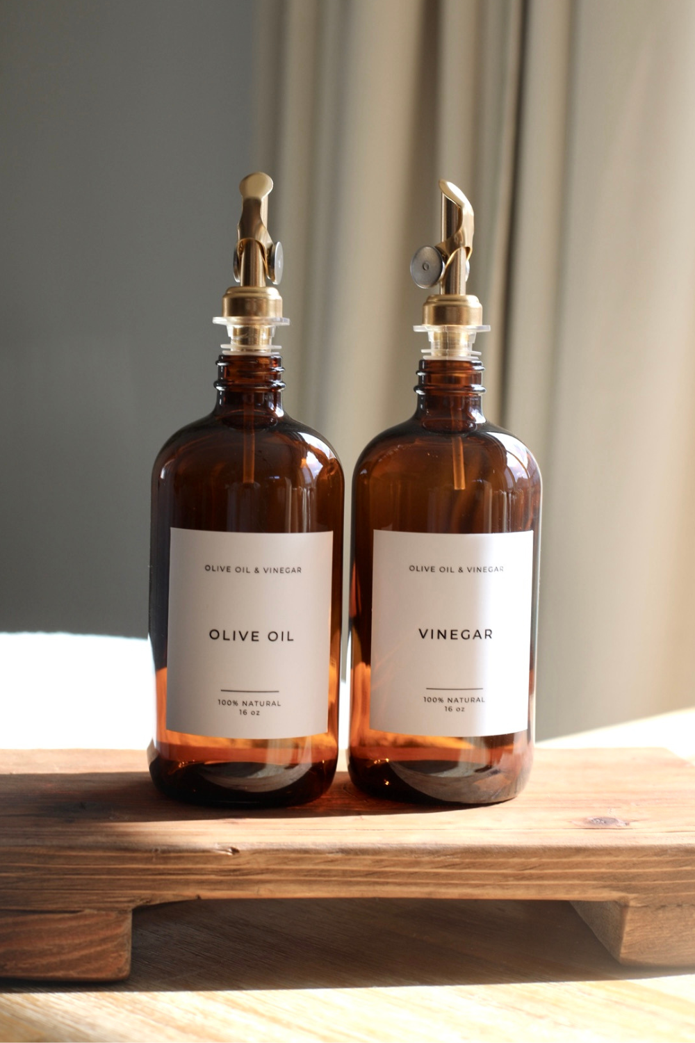 Two brown glass bottles labeled 'Olive Oil' and 'Vinegar' on a wooden surface with a neutral background.