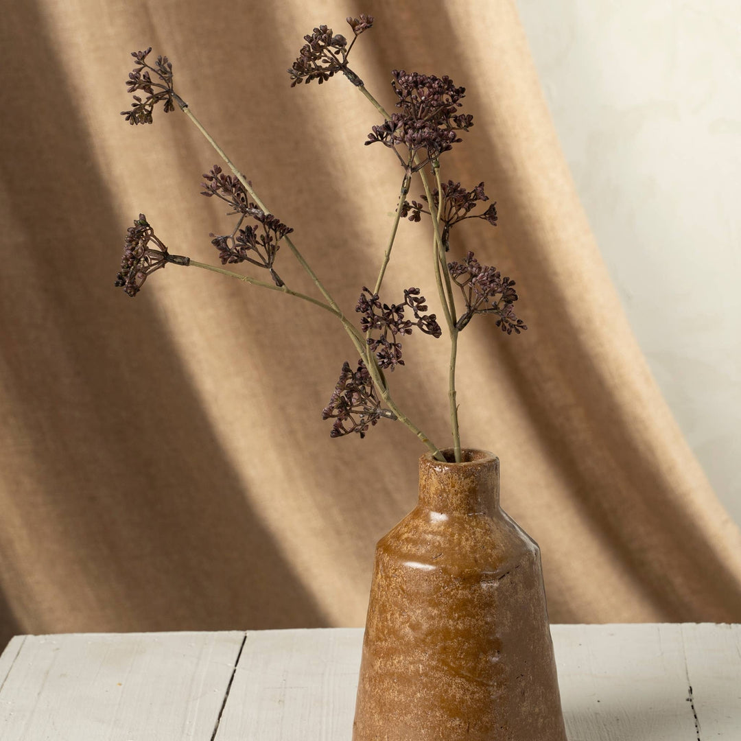 Brown ceramic vase with dried flowers against a beige curtain