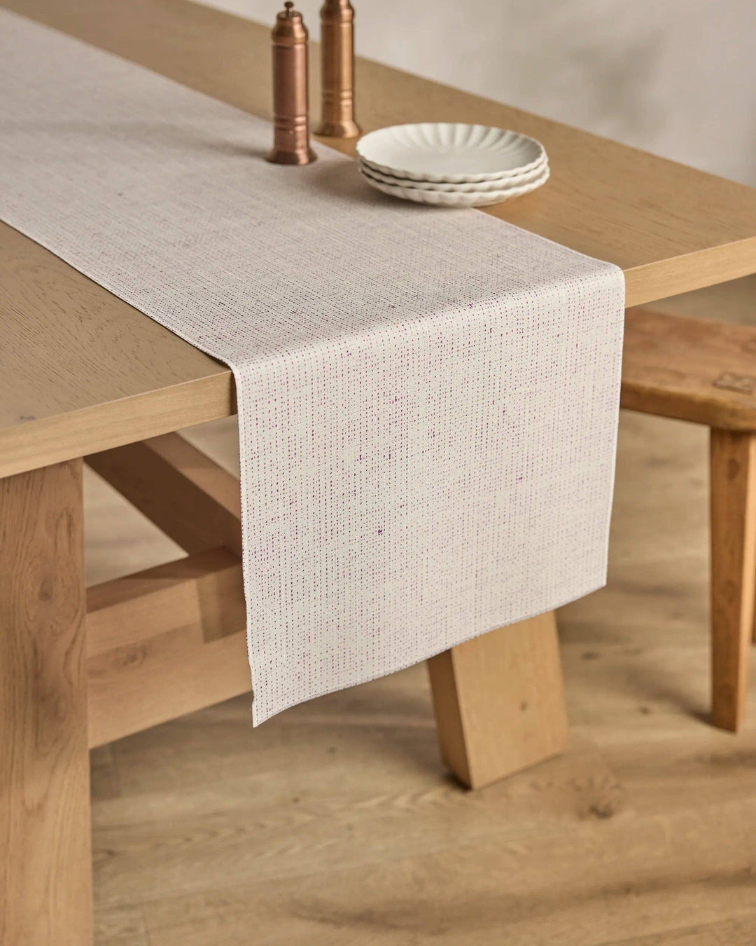 Beige geometry table runner on a wooden table with plates and salt and pepper shakers.