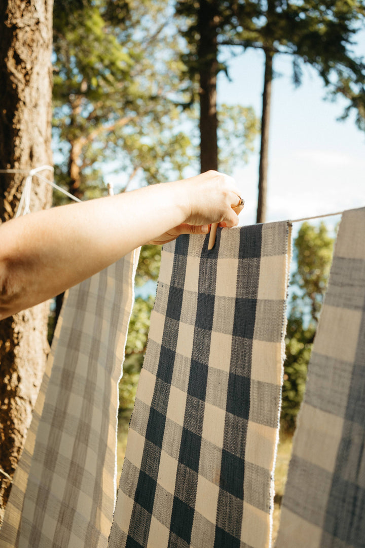 Person hanging checkered table runner on a clothesline with trees in the background