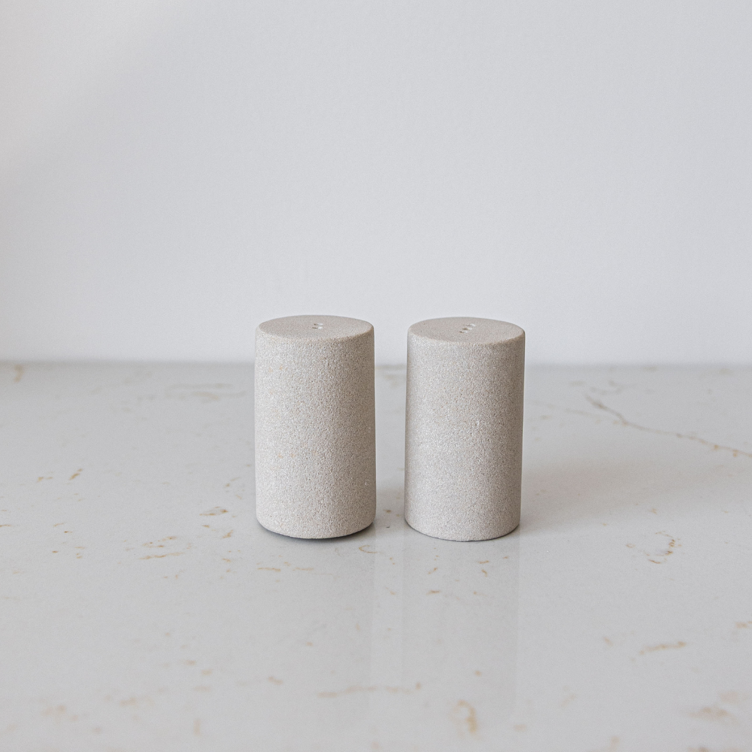 Two cylindrical stone salt and pepper shakers on a light marble surface with a white background