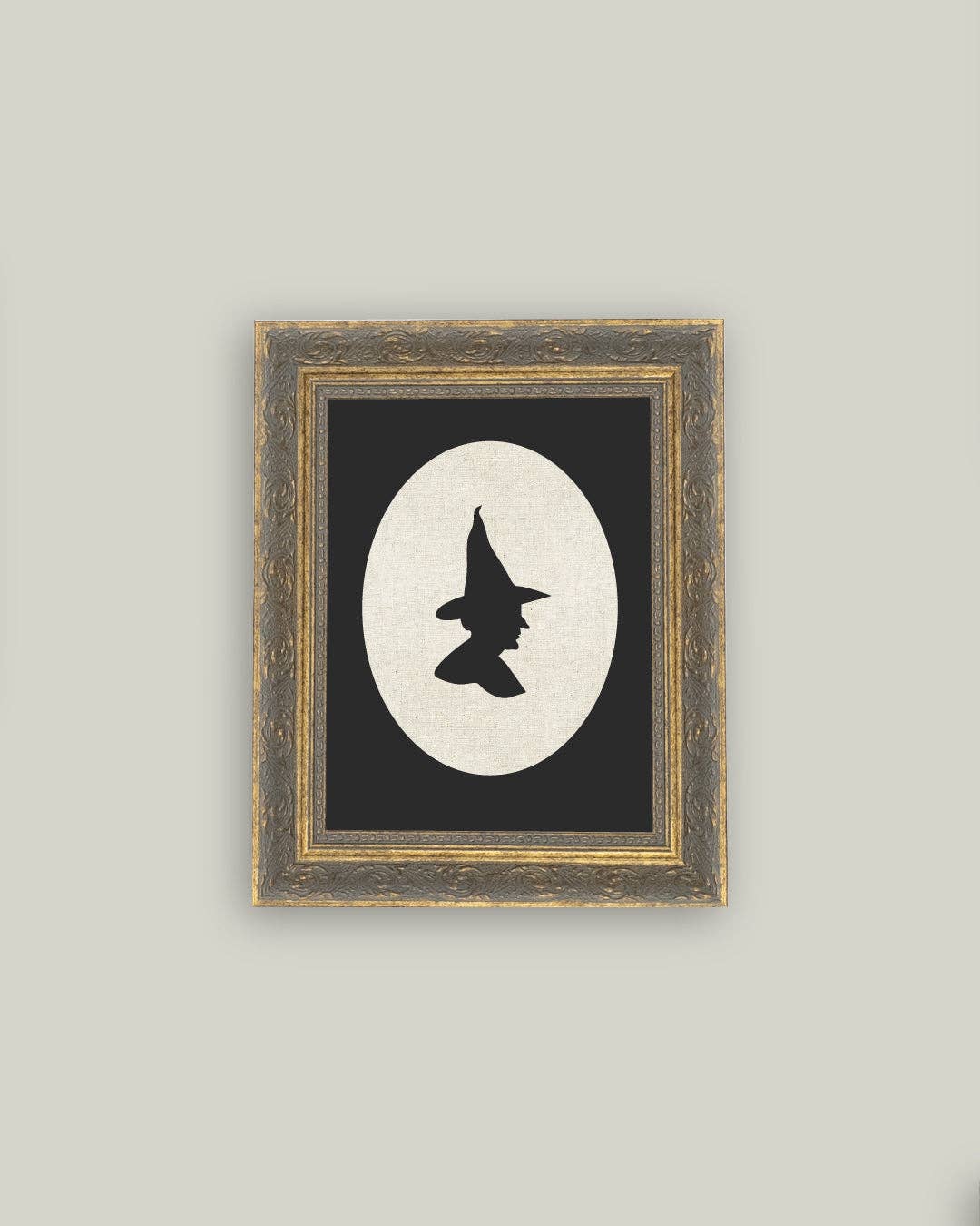 Framed artwork with a black and white silhouette of a witch's hat on a gray wall.
