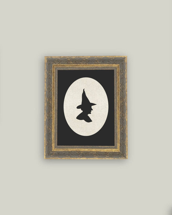 Framed artwork with a black and white silhouette of a witch's hat on a gray wall.