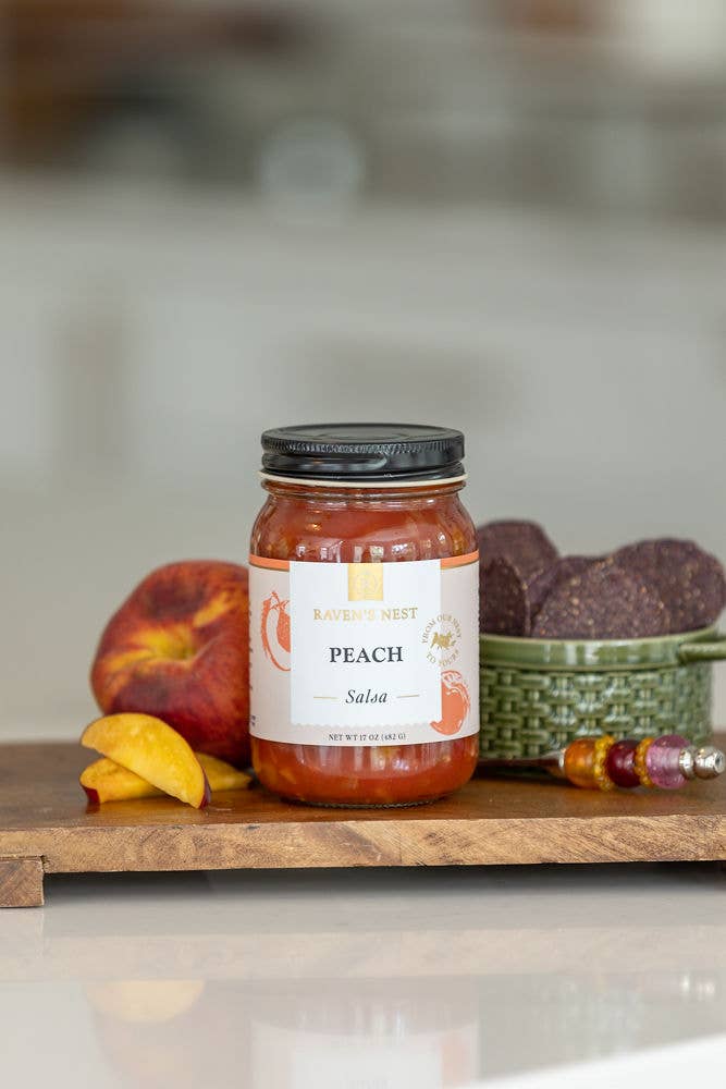 Jar of Peach Salsa on a wooden surface with peaches and tortilla chips.
