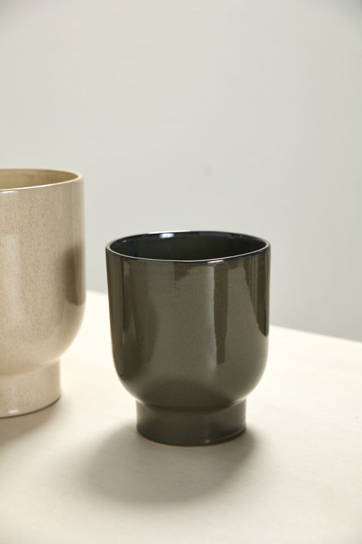Two ceramic cups, one dark green and one beige, on a light surface with a neutral background.