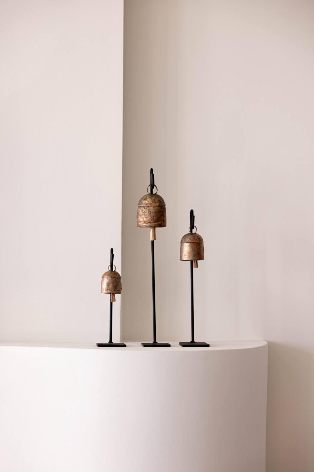 Set of four bronze-colored decorative bells on a white pedestal against a plain wall.