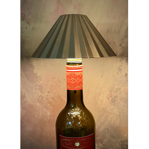 Wine bottle repurposed as a lamp with a striped lampshade on a textured wall background