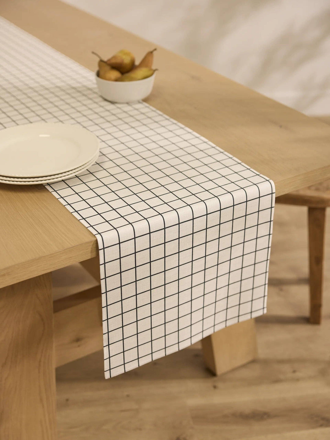 Grid-patterned table runner on a wooden table with a bowl of pears.