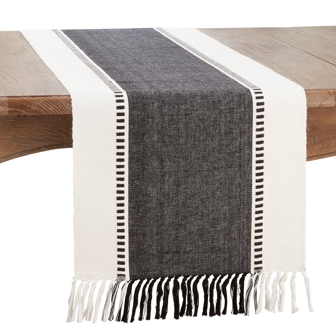 Gray and white striped table runner with fringes on a wooden table.