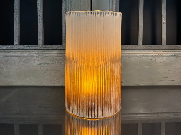 Tall ribbed glass vase with warm glow on a wooden surface