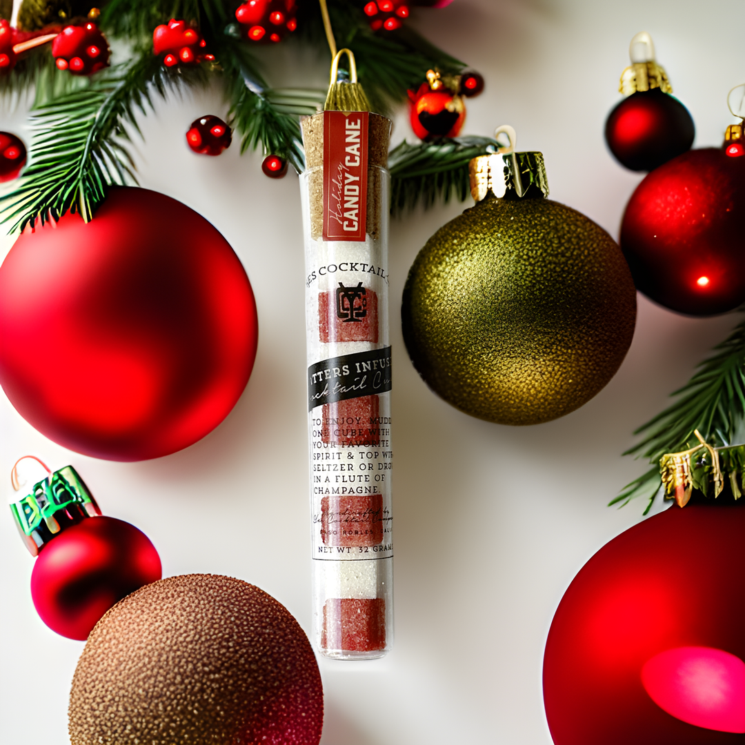 Cocktail mix tube surrounded by Christmas ornaments on a white background