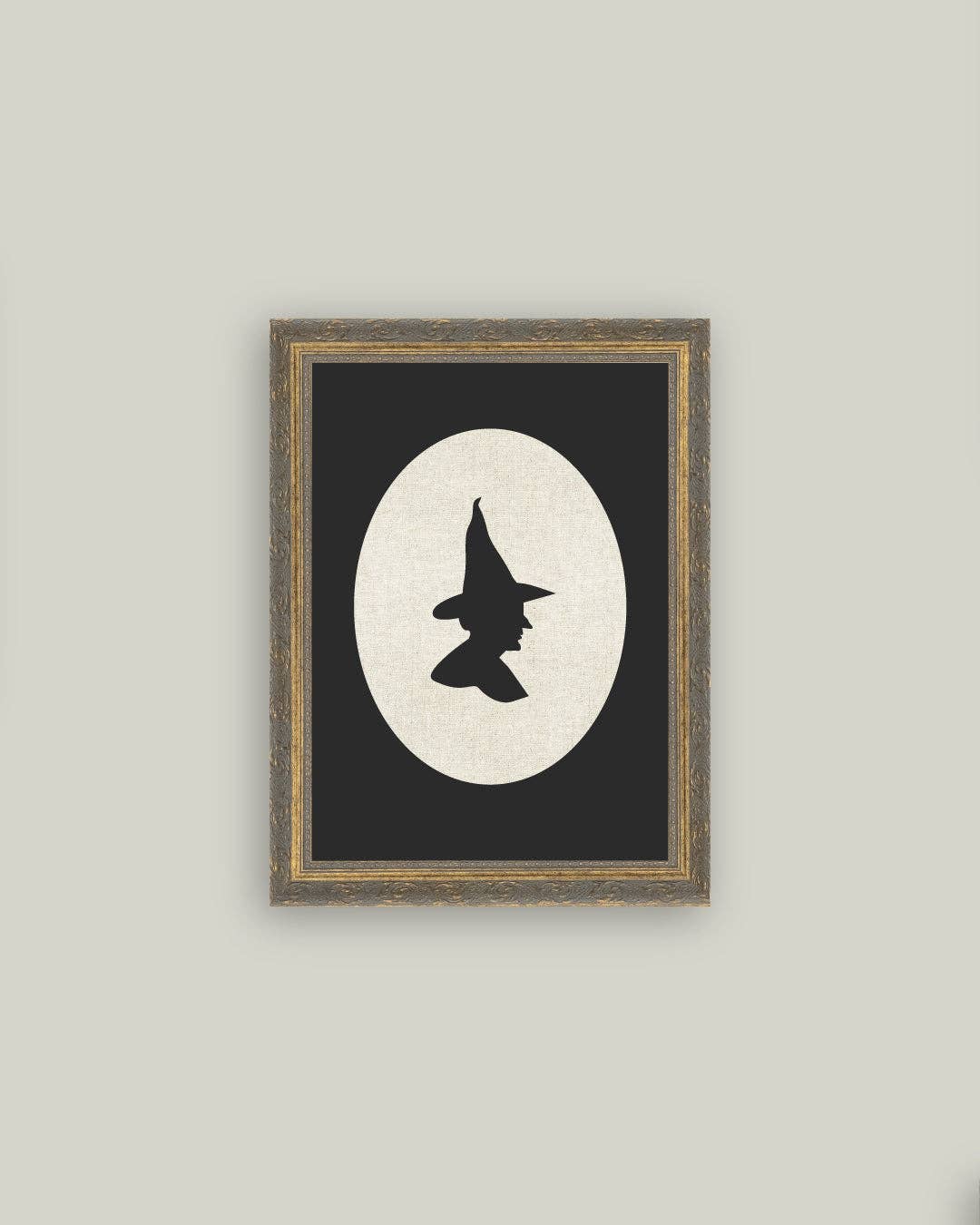 Framed artwork with a witch hat silhouette against a moonlit background on a gray wall.