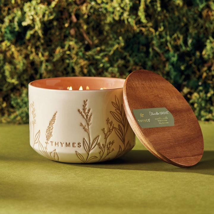 Thymes citronella candle with wooden lid on a green surface with a blurred natural background