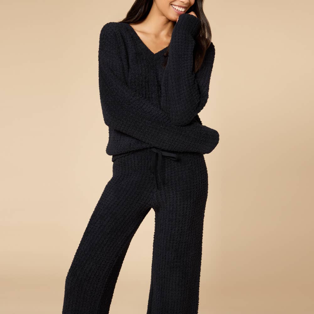 Woman wearing a black ribbed sweater and pants set on a beige background