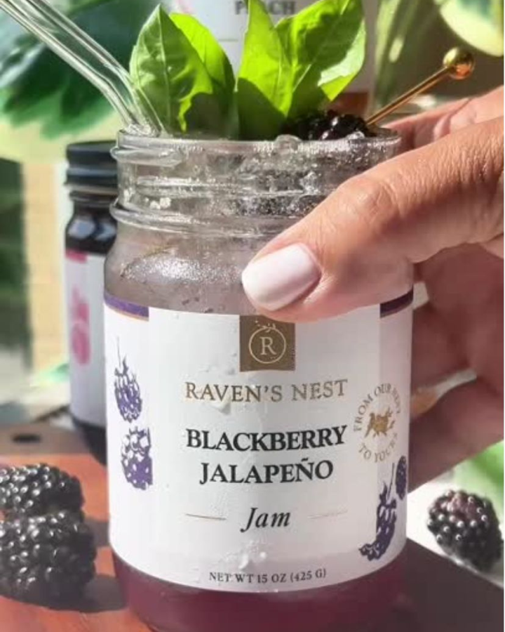 Jar of Raven's Nest Blackberry Jalapeño Jam held by a hand with a blurred background