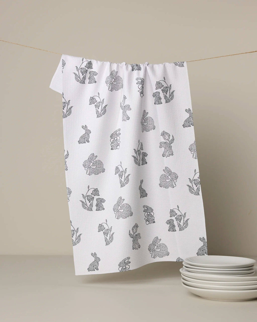 White towel with gray floral pattern hanging on a line against a beige background