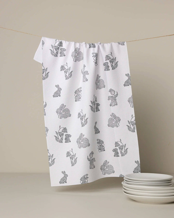 White towel with gray floral pattern hanging on a line against a beige background