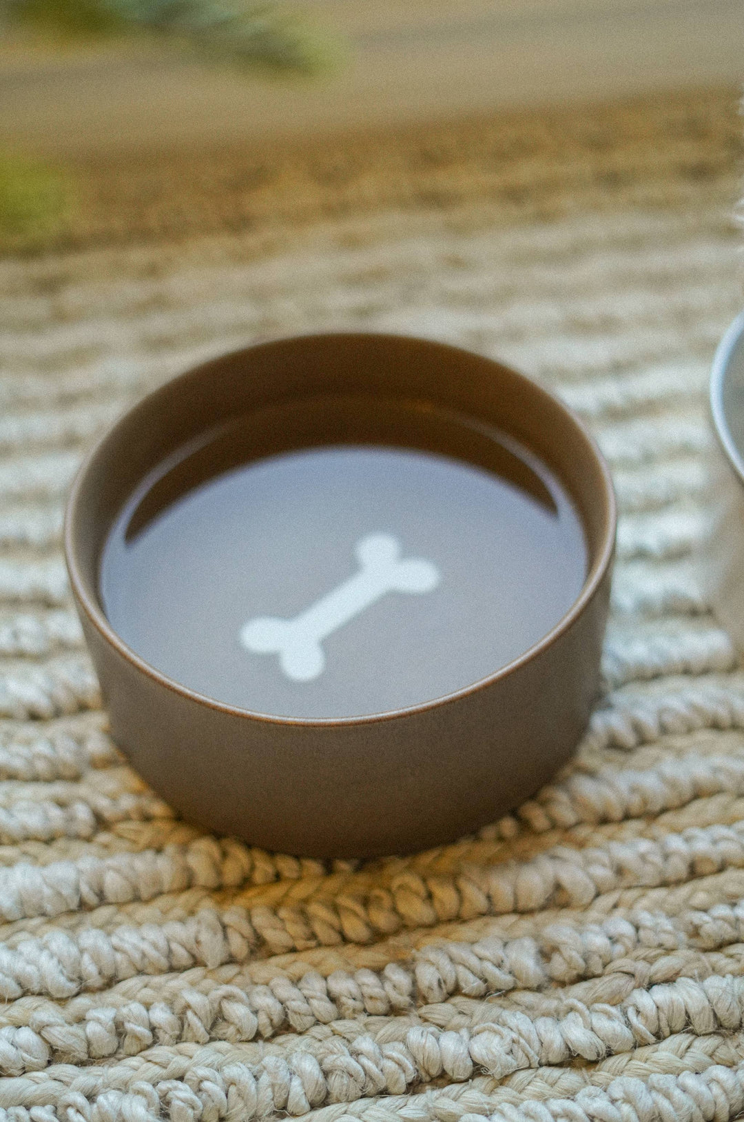 Brown ceramic bowl with a white bone design on a textured beige surface
