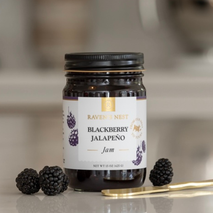Jar of Blackberry Jalapeño Jam from Raven's Nest with blackberries and a spoon on a neutral background