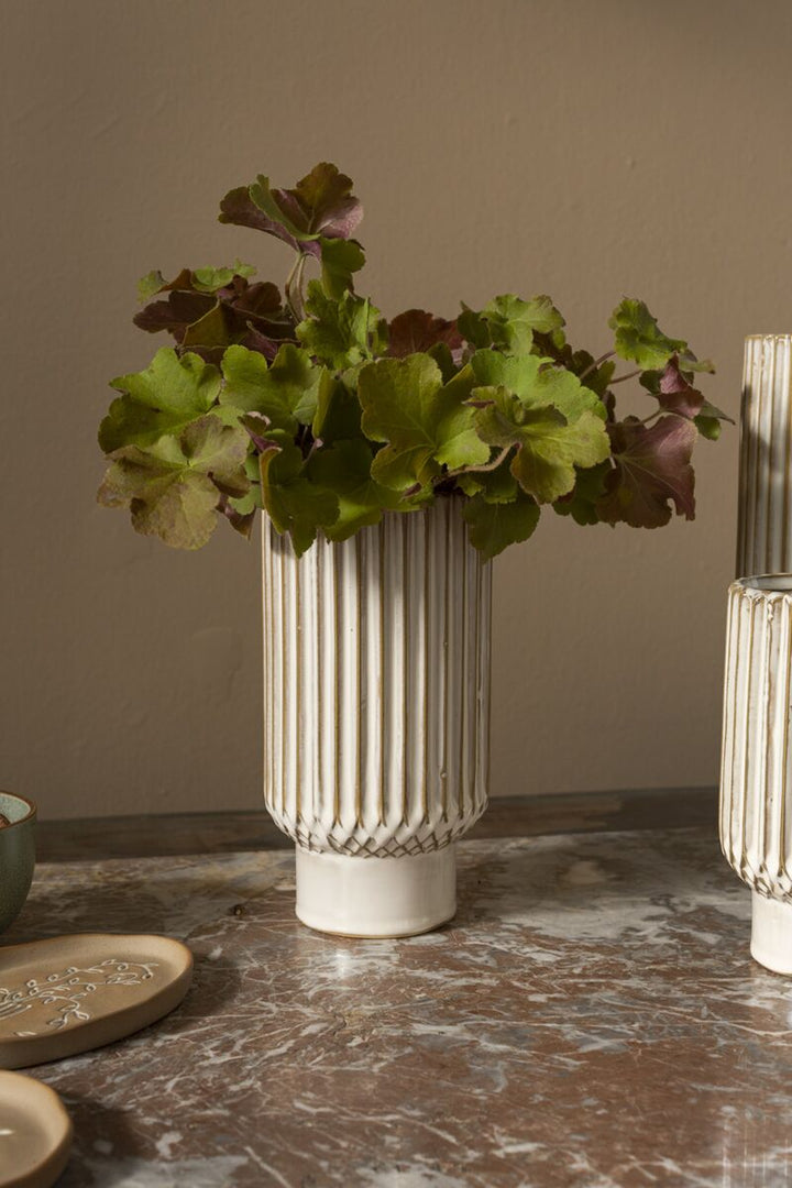 Decorative vase with green foliage on a marble surface against a beige wall
