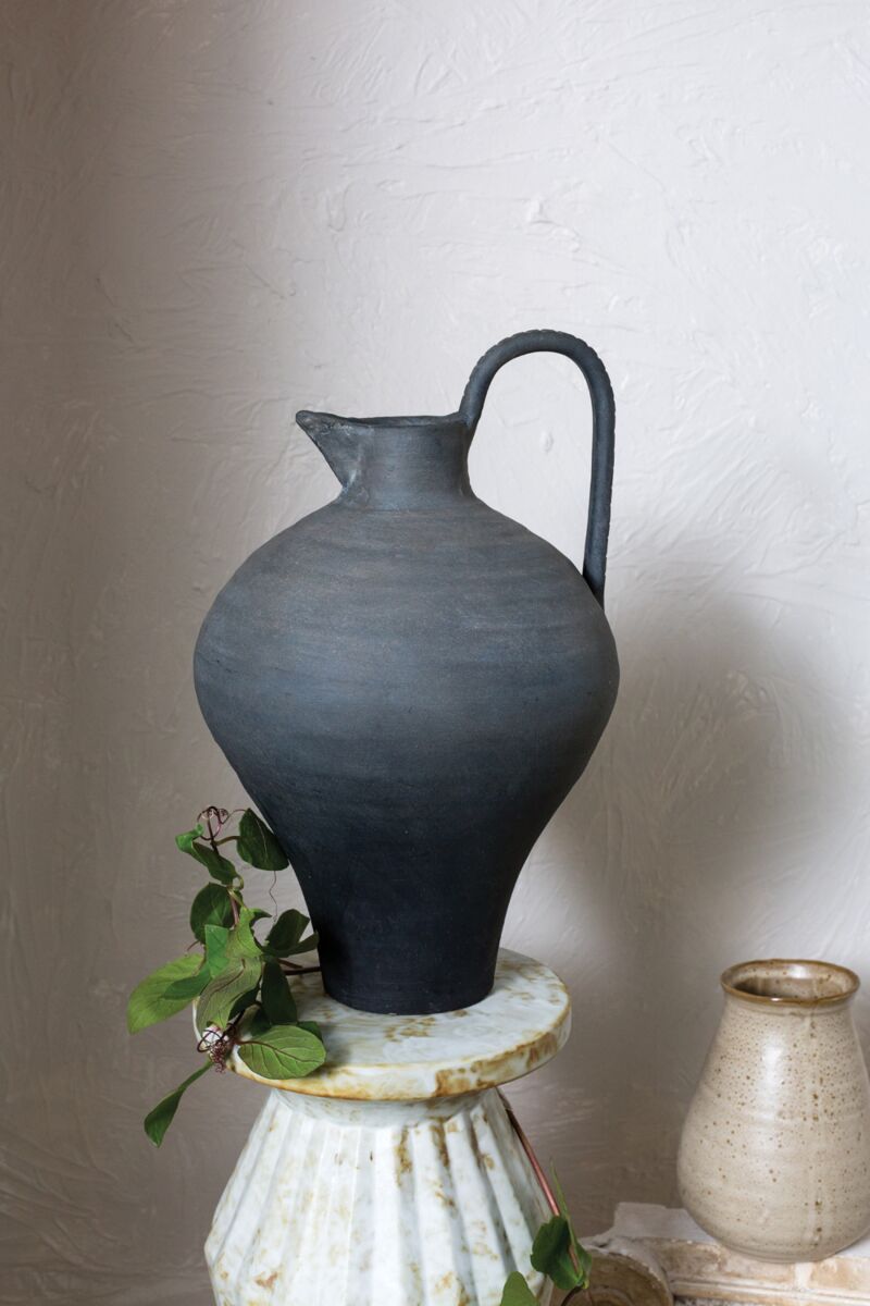 Black ceramic pitcher on a white pedestal with a plain background