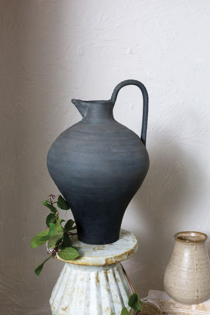 Black ceramic pitcher on a white pedestal with a plain background