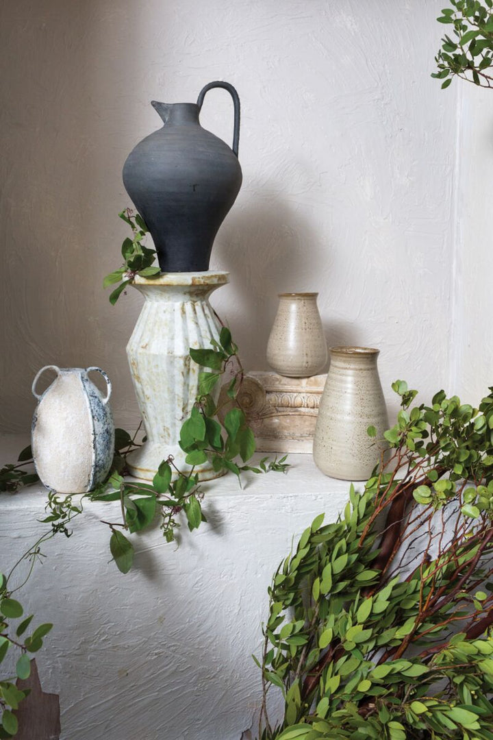 Collection of ceramic vases on a white surface with greenery