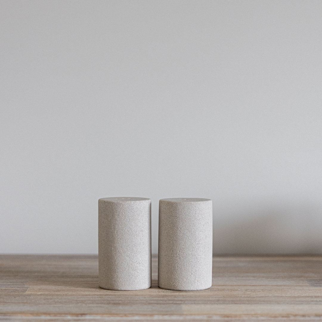 Two cylindrical sandstone salt and pepper shakers objects on a wooden surface with a plain background