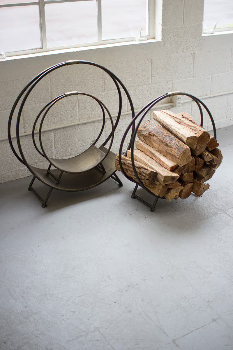 Wooden logs stacked in a metal firewood holder against a white wall with windows.