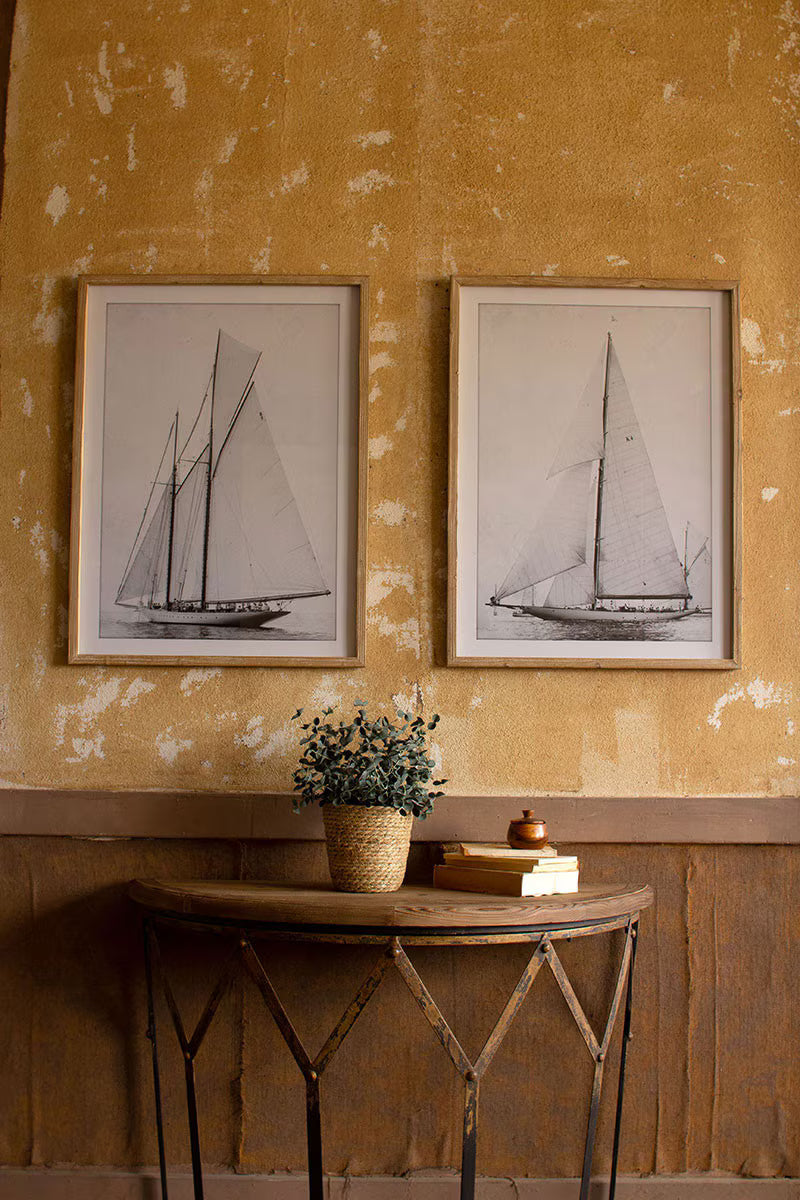 Two framed black and white sailboat prints on a textured yellow wall 