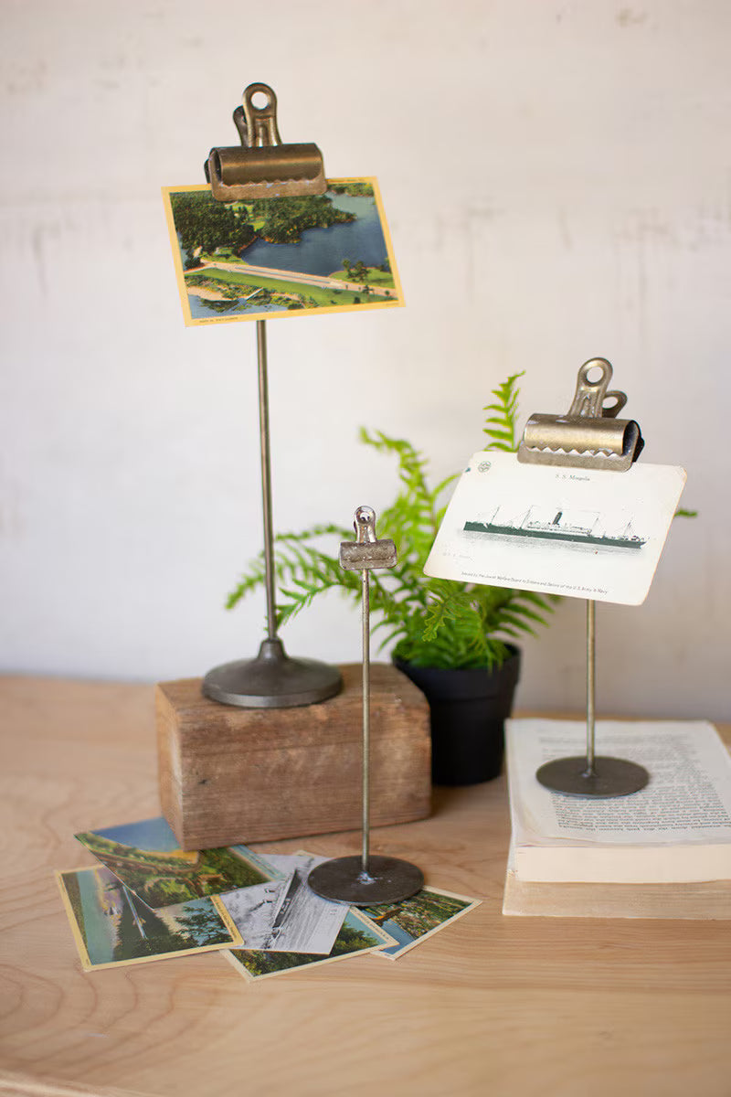 Vintage-style photo stands with clip and stand on a wooden surface with scattered postcards.