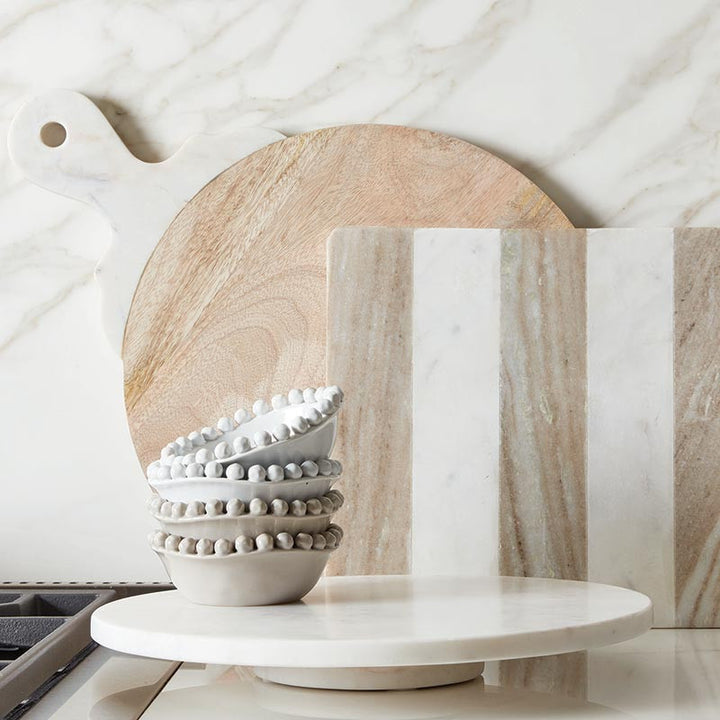 Stack of white ceramic bowls on a marble surface with wooden cutting boards in the background.