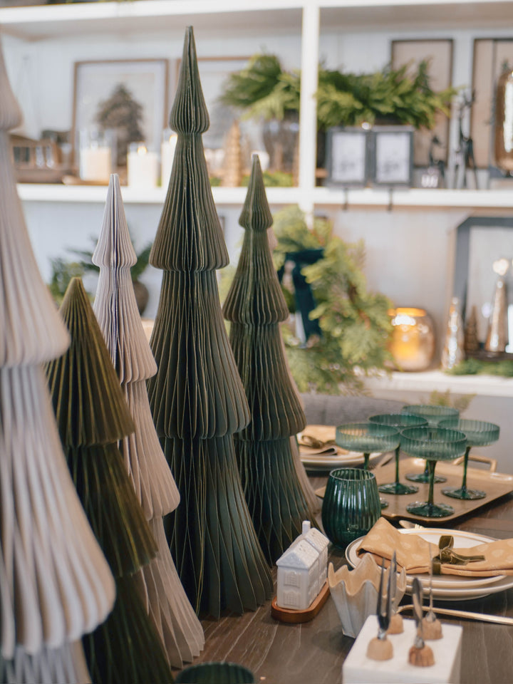 Decorative paper trees on a table with green glasses and candles in a cozy room.